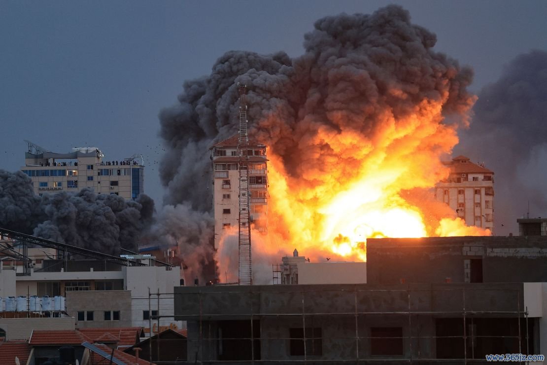 People standing on a rooftop watch as a ball of fire and smoke rises above a building in Gaza City on October 7, 2023 during an Israeli air strike. At least 70 people were reported killed in Israel, while Gaza authorities released a death toll of 198 in the bloodiest escalation in the wider conflict since May 2021, with hundreds more wounded on both sides.